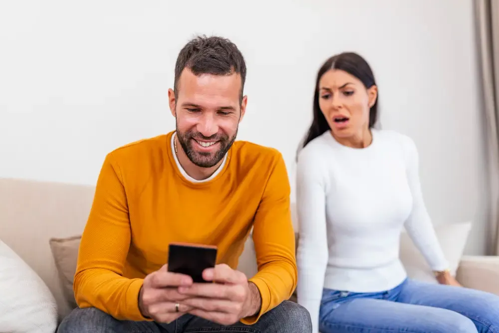 Lonely wife sitting next to husband on his phone